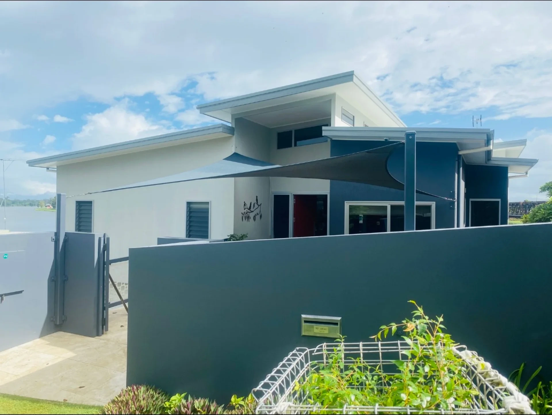 Charcoal shade sail over the entry of a modern riverfront home installed by North Coast Shade